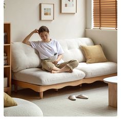 a woman sitting on top of a white couch in a living room next to a window