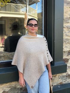 a woman standing in front of a store window wearing a poncho and jeans