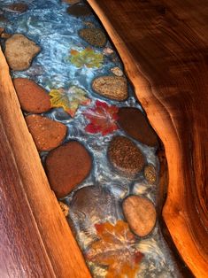 a wooden table with rocks and water in the bottom section, along with leaves on it