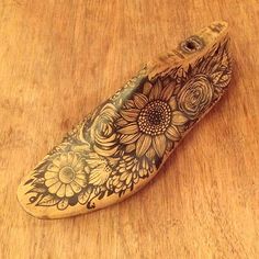 a wooden object with flowers on it sitting on top of a wood table next to a bottle opener