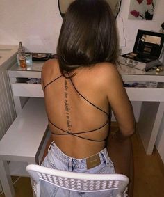 a woman sitting at a desk with her back to the camera and writing on her tattoo