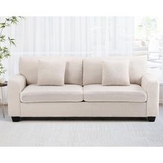 a white couch sitting in front of a window next to a table with a potted plant