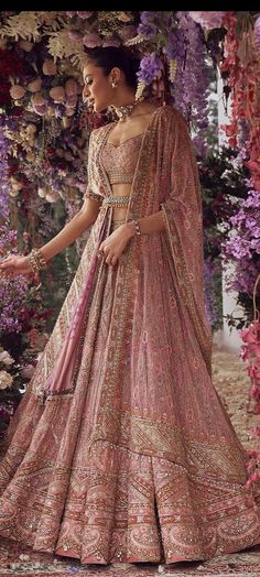 a woman in a pink lehenga standing next to flowers