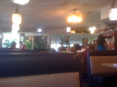 people sitting at tables in a restaurant with plants on the wall and lights above them