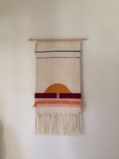 a woven wall hanging with an orange circle on it's side and fringes around the edges