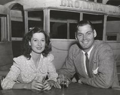 an old black and white photo of two people sitting at a table in front of a bus