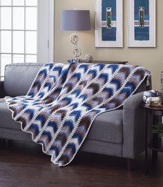 a couch with a blue and white blanket on top of it next to a lamp