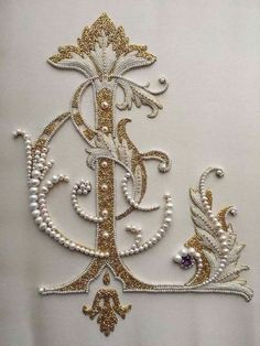 a white and gold embroidered wall hanging with pearls on it's sides, in the shape of a cross