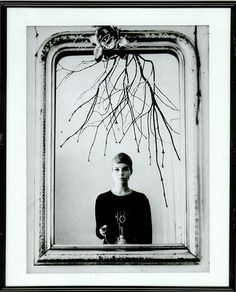 a black and white photo of a woman in front of a mirror with branches on it