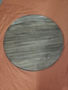 a round wooden table sitting on top of a bed covered in orange sheets and plastic