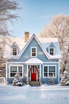 a blue house covered in snow with a red door and wreath on the front porch