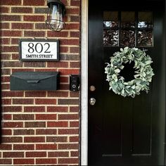 a black front door with a wreath and mailbox on the wall next to it