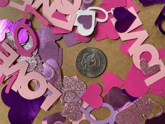 a pile of pink and purple paper cut out letters next to a penny on a table