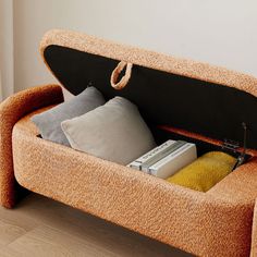 a couch that has some pillows and books in it on top of a wooden floor