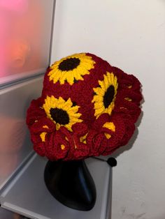 a crocheted hat with sunflowers on it sitting on a black stand