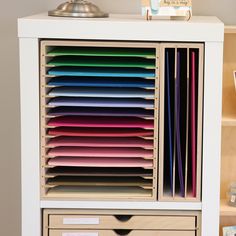 a white cabinet with many different colored papers in front of it and a lamp on top