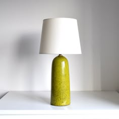 a green lamp sitting on top of a white table next to a white light bulb