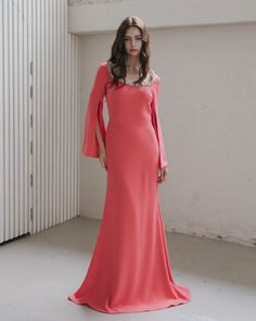 a woman in a long pink dress standing next to a white wall and looking at the camera