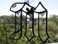 a stained glass wind chime hanging from the side of a window with trees in the background