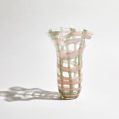 a pink and green glass vase sitting on top of a white table next to a shadow