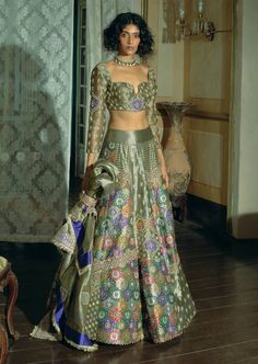 Embrace timeless elegance with this classic kalidar lehenga set, crafted from grey silk zari tissue and jacquard silk banarasi. Featuring jharokha-inspired panels and intricate floral embroidery with zari and zardozi work, the design is enhanced by dabka, sequins, pearls, and gota texturing. The ensemble includes a heavily embroidered choli-cut blouse with full sleeves, adorned with pearl tassels. Complemented by a shimmering grey tissue dupatta with floral embroidered motifs and a detailed border, this set creates a gracefully defined and sophisticated silhouette. Luxury Brocade Sets For Diwali, Blouse With Full Sleeves, Tissue Lehenga, Tissue Dupatta, Pearl Tassels, Cut Blouse, Zardozi Work, Embroidered Motifs, Gray Silk