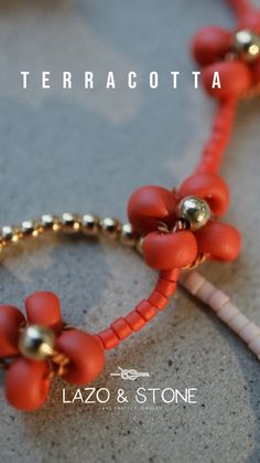 an orange bracelet with gold beads and flowers on the end is shown in front of a white background