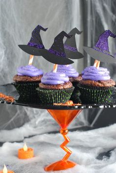 cupcakes with purple frosting and witches hats on top are sitting on a cake stand