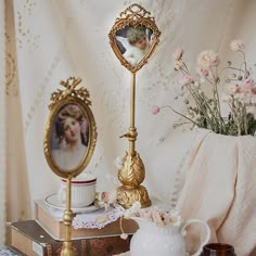 a table topped with books and a vase filled with flowers next to a mirror on top of a wooden table