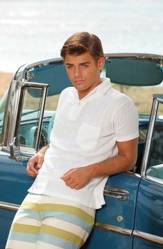 a man sitting on the hood of a car wearing colorful striped pants and white shirt