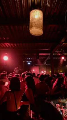 a group of people sitting at tables in a room with red lights on the ceiling