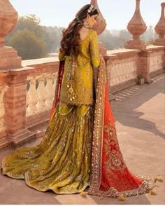 a woman in a yellow and red dress standing on a bridge with her back to the camera