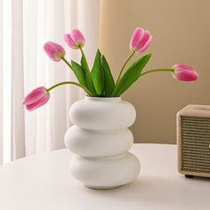 a white vase filled with pink flowers on top of a table next to an old radio