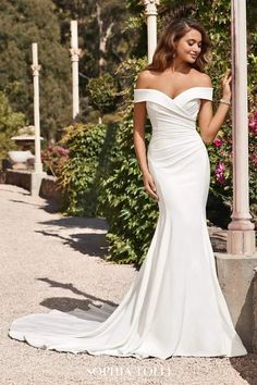 a woman in a white wedding dress standing next to a light pole and flowers on the ground