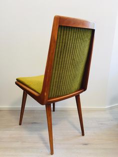 a wooden chair with green upholstered seat and backrest, against a white wall