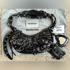 Balenciagarareextra Small Le Cagole Piercing Leather Shoulder Bag, Authentic, Brand New, Never Worn, Color Black, Size 10"W X 6"H X 3"D, Comes With Box, Dust Bag, Authenticity Card And Tag Attached. Retail Price $3,600. Price Firm - No Offers Please. Balenciaga Reimagines An '00s Style With This Hemispherical Shoulder Bag Crafted From Supple Lambskin Leather And Detailed With Edgy Piercing. A Tasseled Zipper Pull, Heart-Shaped Mirror Bag Charm And Zip Pouch Complete The Look With Signature Flair Balenciaga Crystal Bag, Balenciaga Bag Silver, Balenciaga Le Cagole Rhinestone, Balenciaga Sleeve Bag, Balenciaga Le Cagole Pink Rhinestone, 00s Style, City Bag, Balenciaga Bag, Zip Pouch