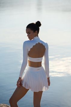 a woman standing on the beach wearing a white dress and high heeled shoes with her back to the camera