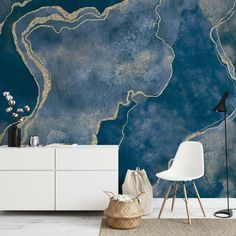 a blue and gold wall mural in a room with a white dresser, chair and lamp