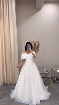 a woman taking a selfie wearing a white wedding dress with off the shoulder sleeves