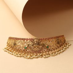 Description Traced in a vintage antique-gold base, this classic antique choker represents traditional temple design jewelry in timeless aesthetics. The choker is carved all over with Laxmi motif surrounded with florals and peacocks to match the outfit of an Indian bride. Choose this for your special event and feel the regality of artisanship. Details & Specifications: Materials used : Brass Alloy with Antique Gold Plating Weight – Choker 62.2 gm, Earrings 22.5 gm Length – Choker 16.5 cm, Earring Antique Choker, Temple Design, Choker Set, Jewelry Choker, Traditional Jewelry, Design Jewelry, Peacocks, Indian Bride, Gold Plating