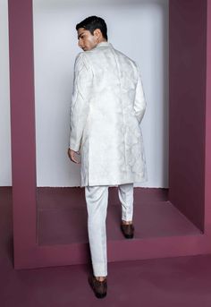 Embrace sophistication with a dull gold embroidered Jacquard jacket paired with a front-open kurta featuring fine pleating details on the placket. Complete the ensemble with matching pants, achieving a harmonious blend of opulence and intricate design for a refined and stylish look. Elegant Semi-formal Sets For Eid, Off White Fitted Bandhgala Straight Kurta, Off White Fitted Bandhgala Kurta, Fitted Off White Bandhgala Straight Kurta, Formal Embroidered Off-white Nehru Jacket, Formal Embroidered Off White Nehru Jacket, Formal Off White Bandhgala With Zari Work, Embroidered Off-white Nehru Jacket For Formal Occasions, Off White Sherwani With Chikankari Embroidery For Formal Occasions