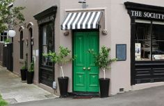 a green door on the side of a building with black and white awnings