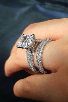 a woman's hand with two wedding rings on top of her finger and the engagement ring