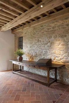 a table with a laptop on it in front of a stone wall and brick floor