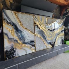 three pieces of art work on display in front of a wall with gold and black designs