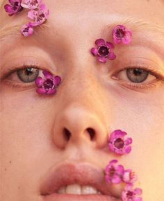 a woman with pink flowers on her face and nose, looking at the camera while she is