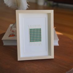 a white frame sitting on top of a wooden table next to a book and feather