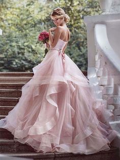 a woman in a pink wedding dress standing on steps with her back to the camera