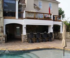 an outdoor patio with chairs and umbrellas next to a swimming pool in front of a house