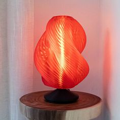 an orange lamp sitting on top of a wooden table next to a white wall and curtain