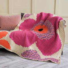 a crocheted blanket with an orange and pink flower on it sitting on a couch